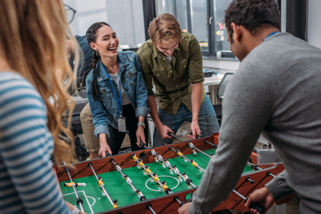 Building Trust in the Workplace by Improving Employee Well-Being Canva happy multicultural people playing in table soccer at modern office scaled 1